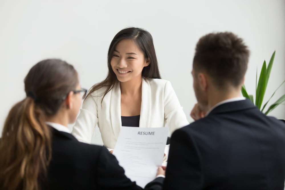 happy smiling woman in white top sits before two people in dark business suits during hiring process making a choice for hire