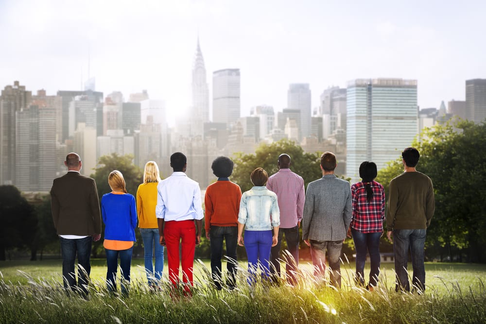 high concept abstract of a group of business and casual people with backs turned away staring into the bright sky and a skyline of city