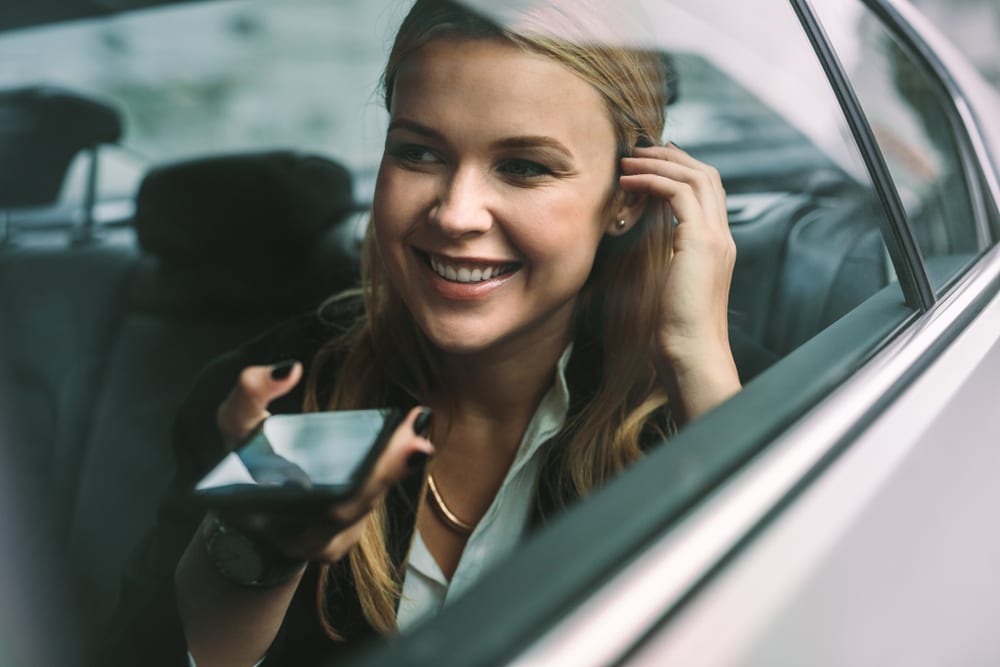 young adult sitting in the backseat of a car vehicle talking on phone to virtual assistant asking for details about business clothes