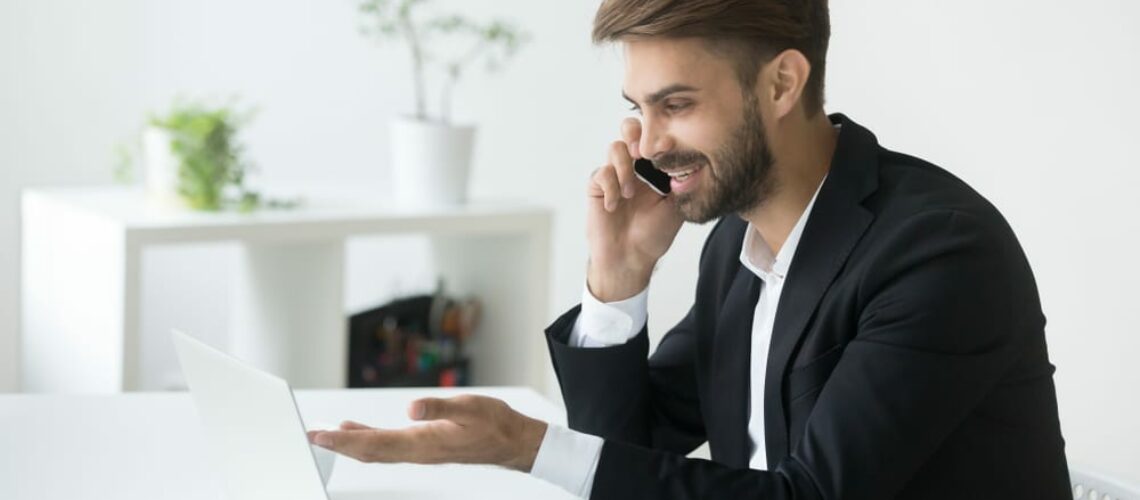 man in business suite smiling at computer screen happy about making a sale and money finances in immaculate clean office