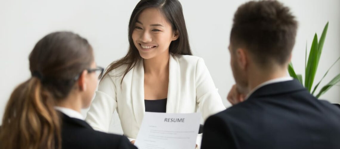 happy smiling woman in white top sits before two people in dark business suits during hiring process making a choice for hire