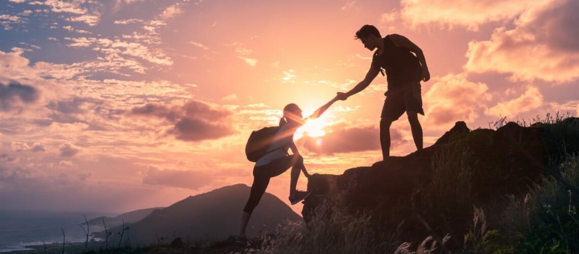 two people hiking climbing mountains during sunset sunrise helping each other lending hand