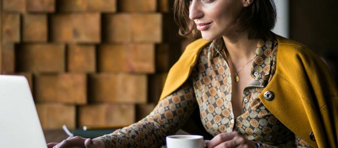 woman holds cup of espresso in mustard sweater